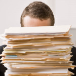 Overworked, frustrated businessman looking at pile of file folders